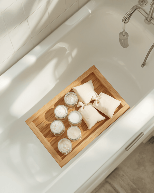 Bath soaks and mineral salts arranged on a wooden bath tray beside a tub